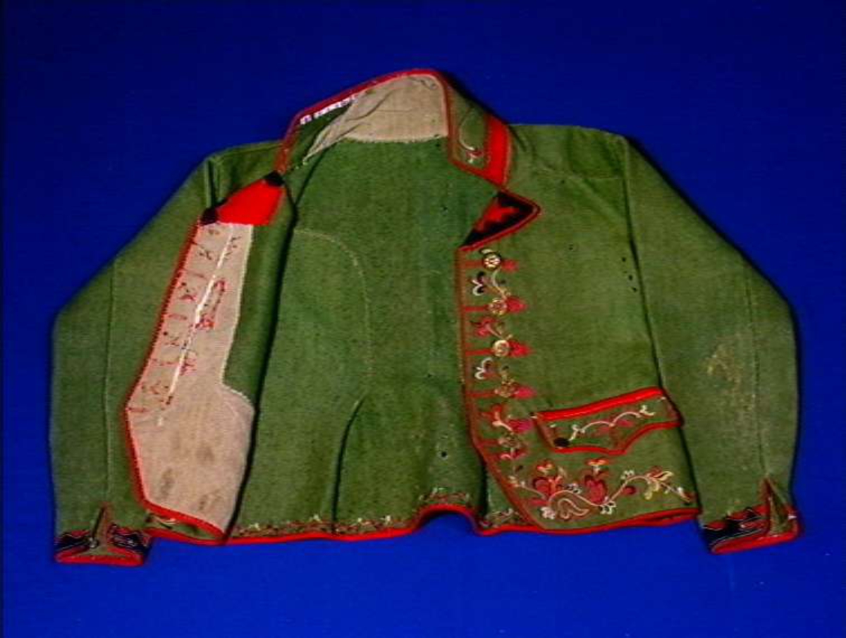 Grønn trøye med flerfarget ullgarns broderi som dekor og rød kanting.