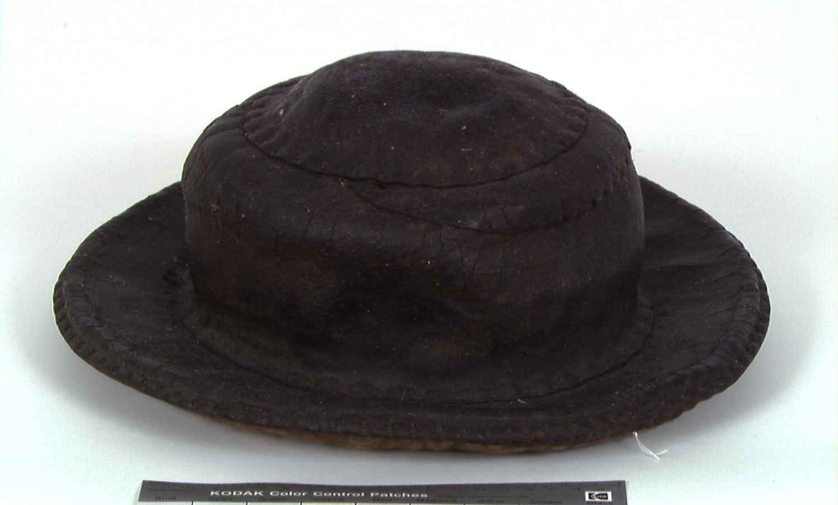 Rund hatt med brem. Sydd med lærbånd. Toppen av hatten er laget med to mindre biter av lær, antakelig en reparasjon. Foret er laget av tovede fibre.