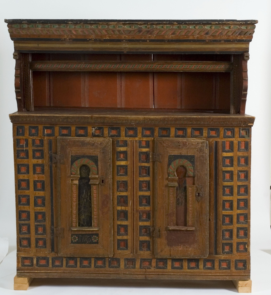Skap i to deler. Høy skjenkebord, lav overdel. Skåret dekor i gesims med dragehoder i konsollene. Kassetter med rammefyllinger som dekor i frontpanelene. På dørene er det også malte motiv innen romanske buer. På høyre dør malte bygninger, på venstre dør er motivet uleselig. Ådret på sidene.