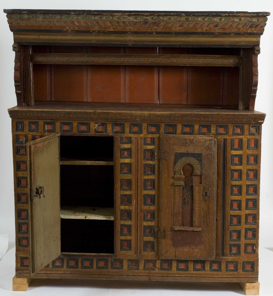 Skap i to deler. Høy skjenkebord, lav overdel. Skåret dekor i gesims med dragehoder i konsollene. Kassetter med rammefyllinger som dekor i frontpanelene. På dørene er det også malte motiv innen romanske buer. På høyre dør malte bygninger, på venstre dør er motivet uleselig. Ådret på sidene.