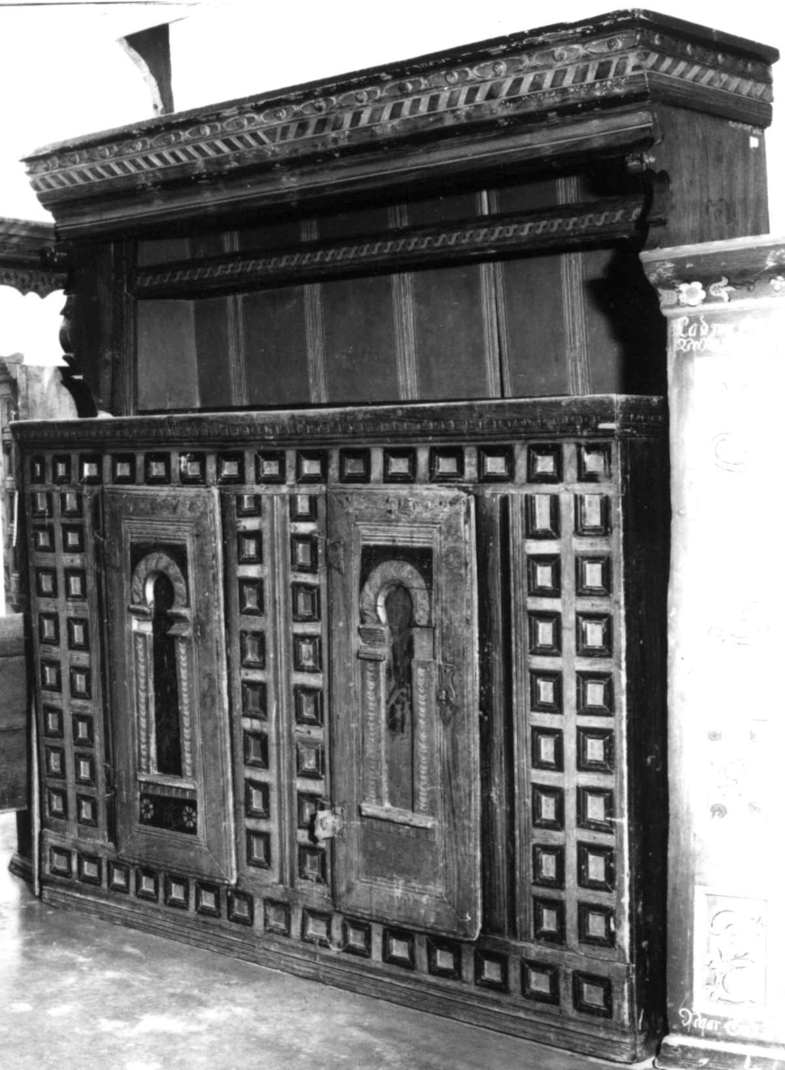 Skap i to deler. Høy skjenkebord, lav overdel. Skåret dekor i gesims med dragehoder i konsollene. Kassetter med rammefyllinger som dekor i frontpanelene. På dørene er det også malte motiv innen romanske buer. På høyre dør malte bygninger, på venstre dør er motivet uleselig. Ådret på sidene.