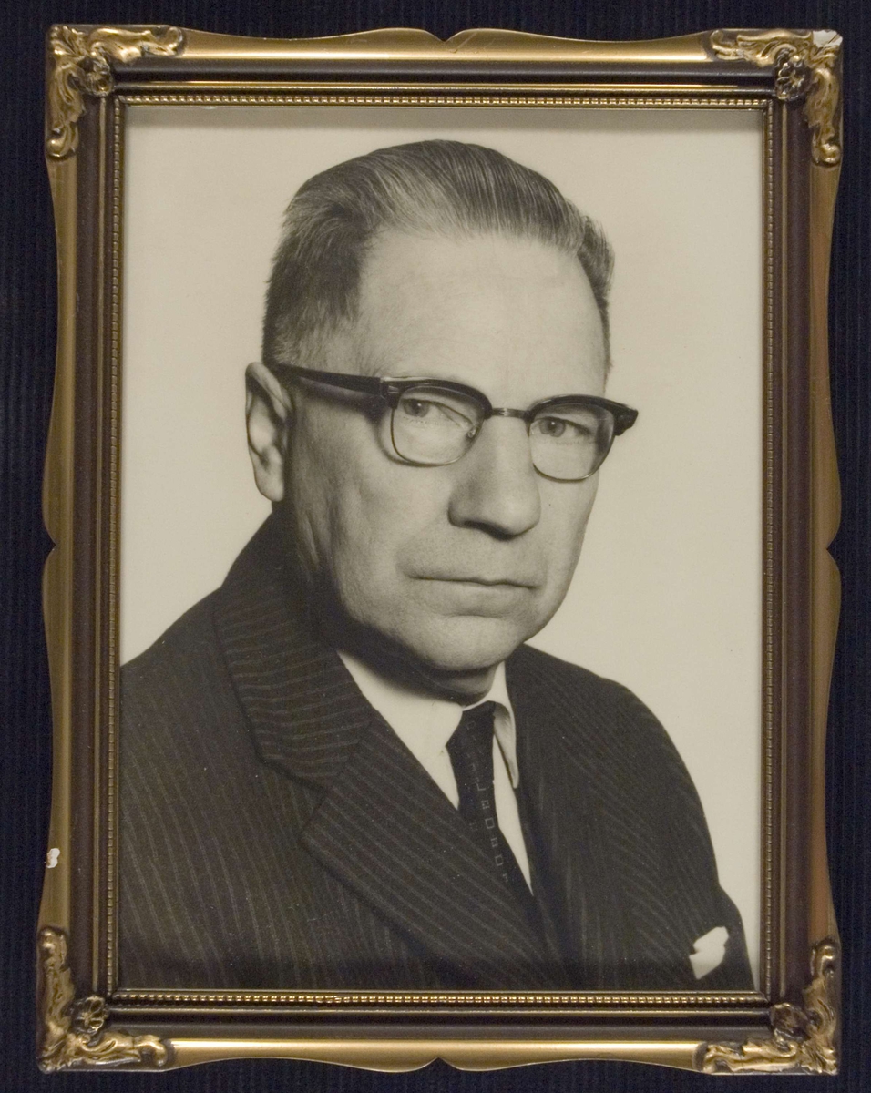 Portrett av apoteker Fritjof Lambert Myhre, med briller, iført dress, hvit skjorte og slips.
