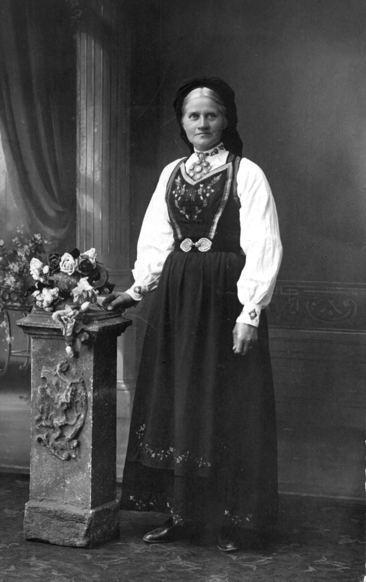 Asgjerd O. Haugen (1861-1937) fra Fyresdal, Telemark, ansatt i oppsynet på NF 1894 -1936. På bildet poserer hun i fotoatelier, kledd i kvinnedrakt fra hjemstedet.