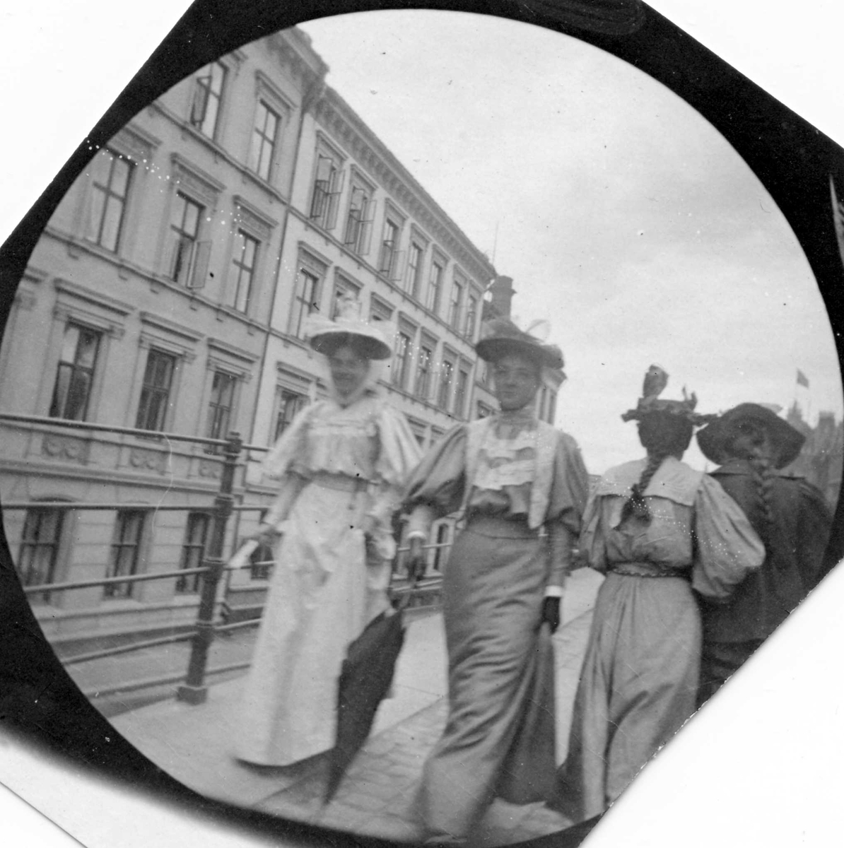 Frk.Bjelke og frk. Hvoslef spaserer langs gjerde i bygate, Oslo. To damer med ryggen til og bygårder.