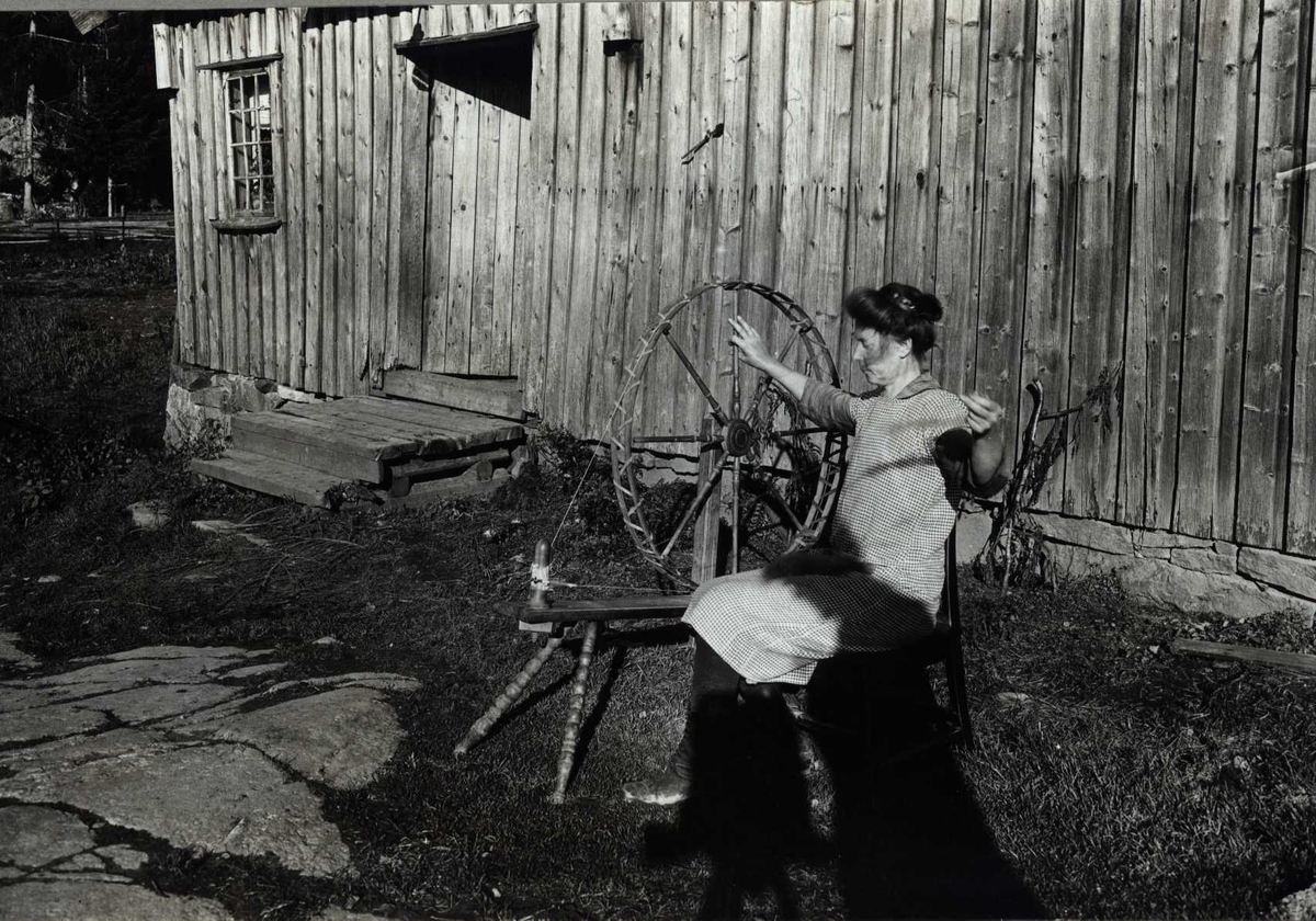 Anne Grimsrud spinner på skotrokk utenfor et hus. Nordby, Ås, Akershus 1929.