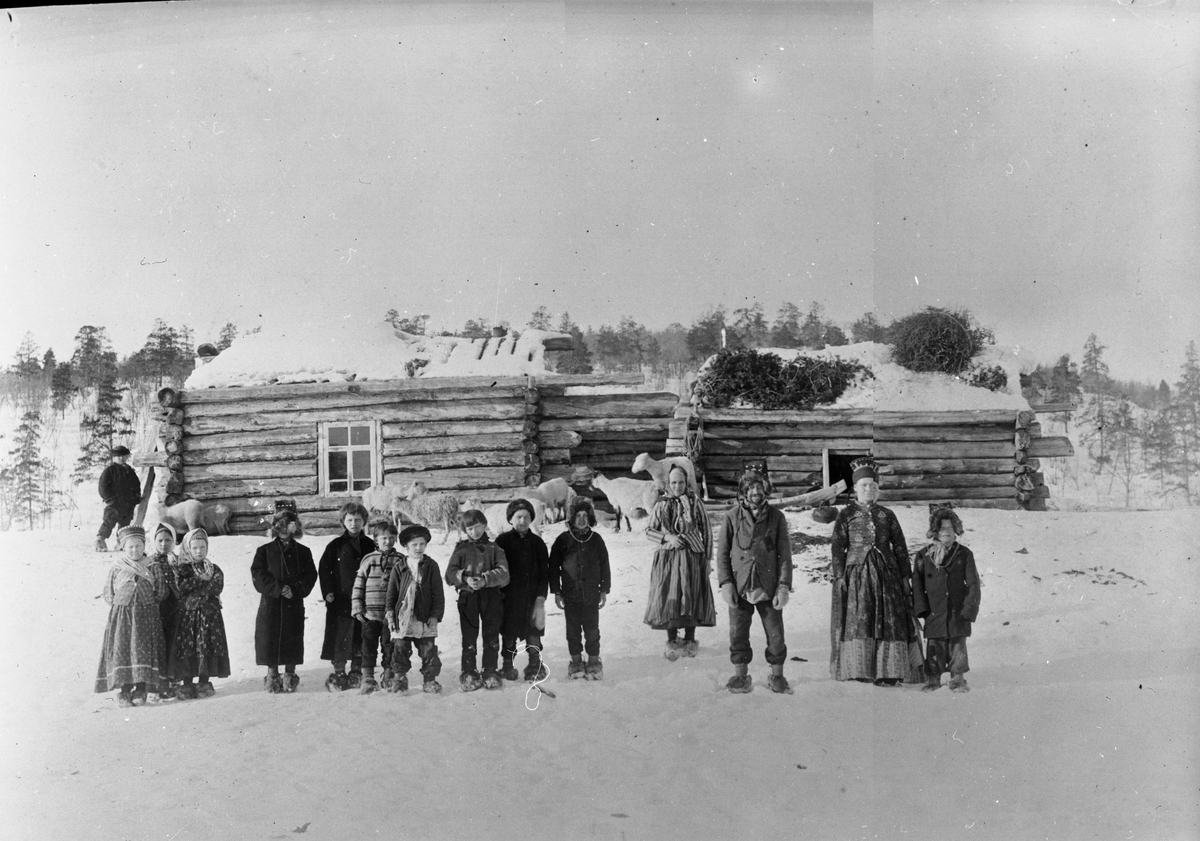 Skoltesamer, voksne og barn, utenfor en bygning i Boris Gleb, Russland eller Øvre Skolteby, Sør-Varanger, Finnmark, før 1897.