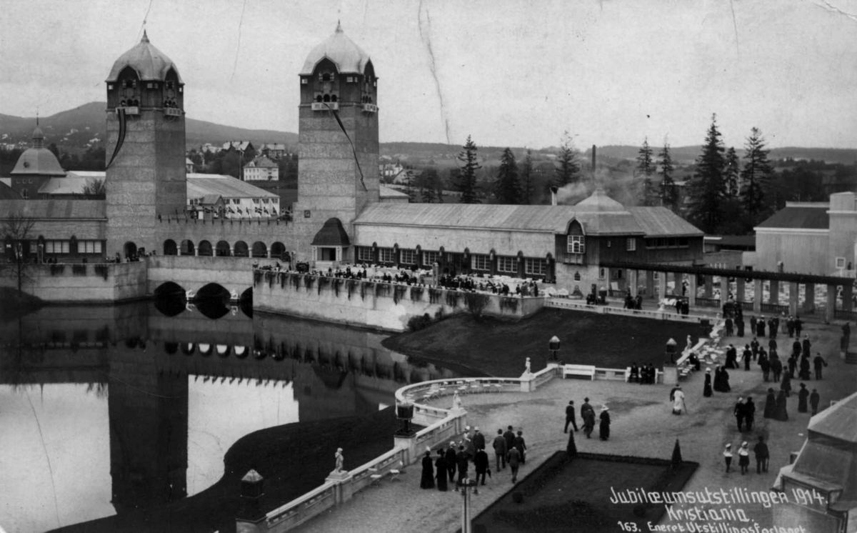 Jubileumsutstillingen på Frogner, Oslo, 1914. Oversiktsbilde over utstillingsområdet med to tårn i bakgrunnen. En dam i midten. Spaserende på veiene rundt dammen.