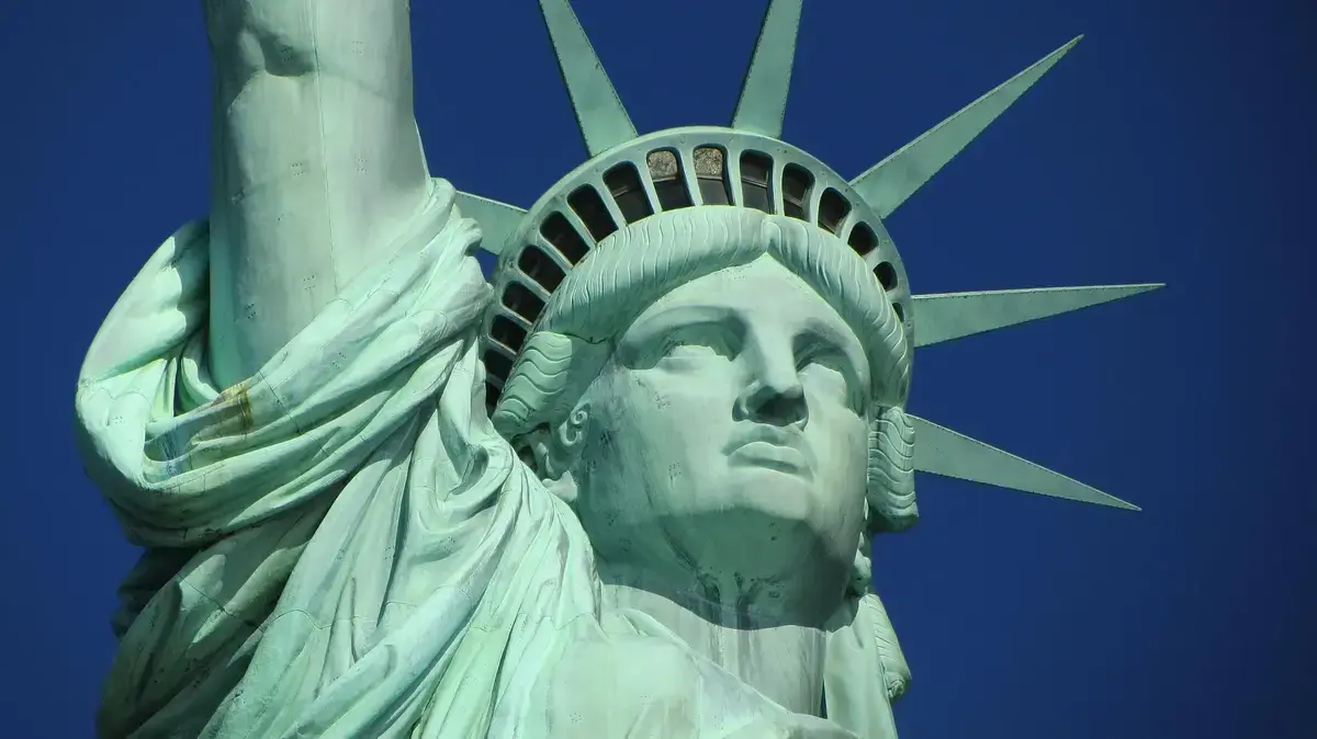 Hodet og en del av overarmen til statuen Frihetsgudinnen iNew York. Grønnfarget statue mot blå himmel.