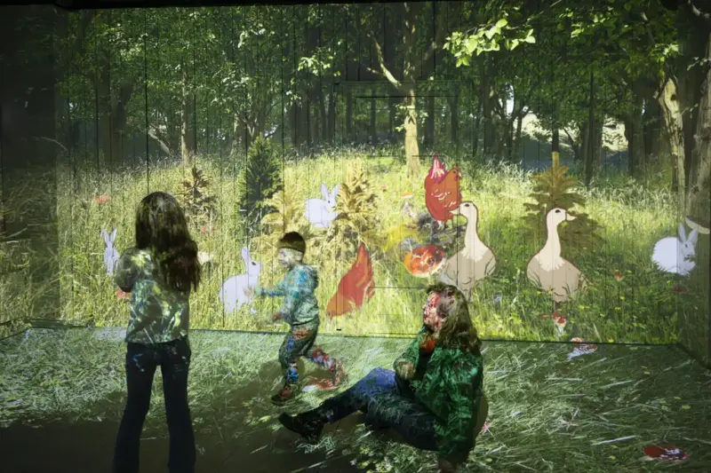 Voksen og to barn opplever en projeksjon av skog og dyr i Ibsens Museum & Teater.