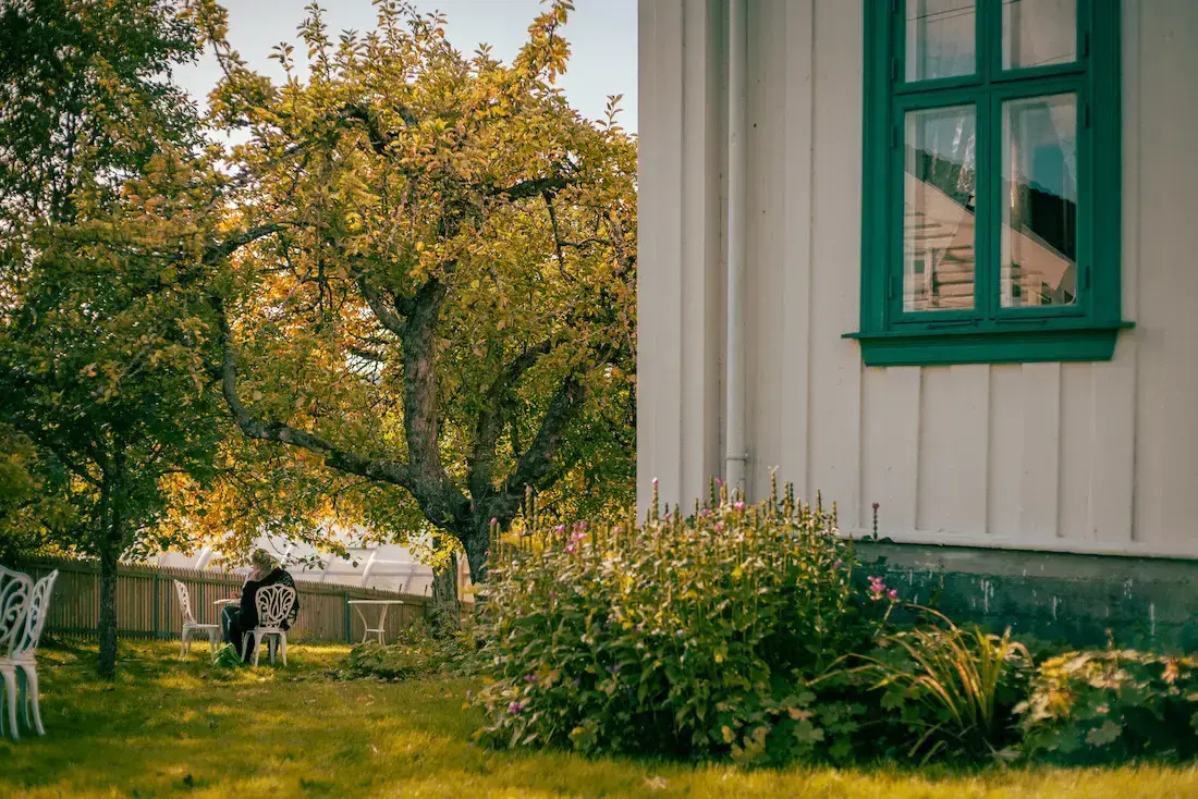 Hushjørne med frodig hage og en person som sitter ved et cafebord.