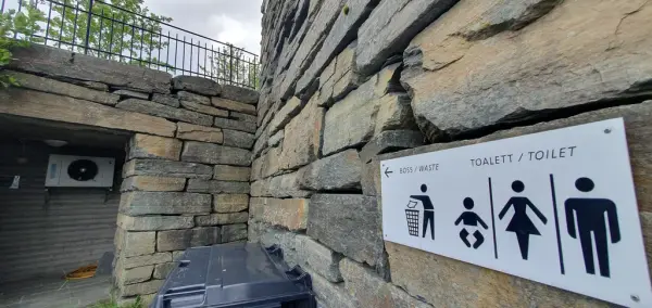 Murvegg med skilt som viser til toalett på utsida av informasjonsbygget