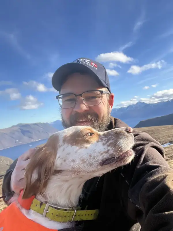 Selvportrett av Mann med caps og briller. Hand holder rundt en hund 