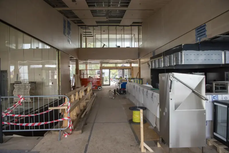 Til høyre: restaurantkjøkken i stål monteres. Rett fram: hovedinngangen med glassgang i kontorfløyen over. Til venstre: nedgang til garderobe, sikret med provisorisk gjerde.